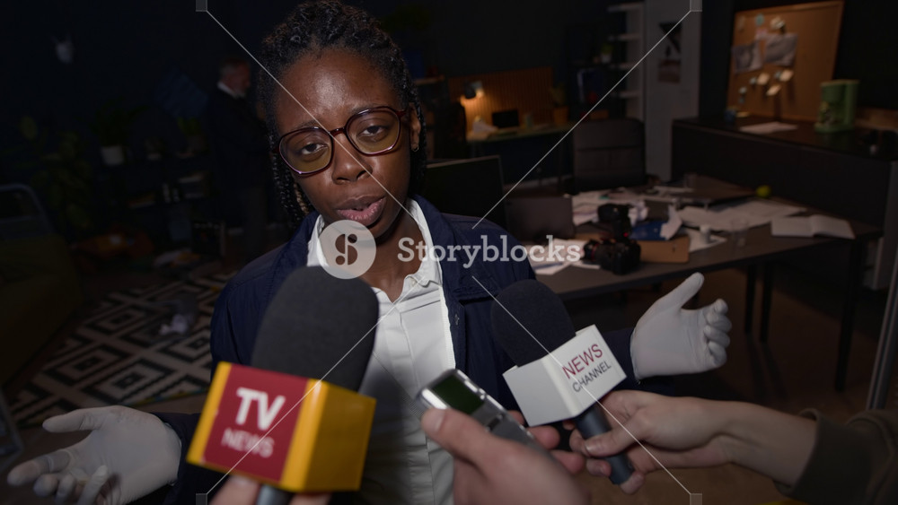 Medium shot of young confident Black female police officer commenting on crime case, answering questions of press interviewing her at crime scene in office