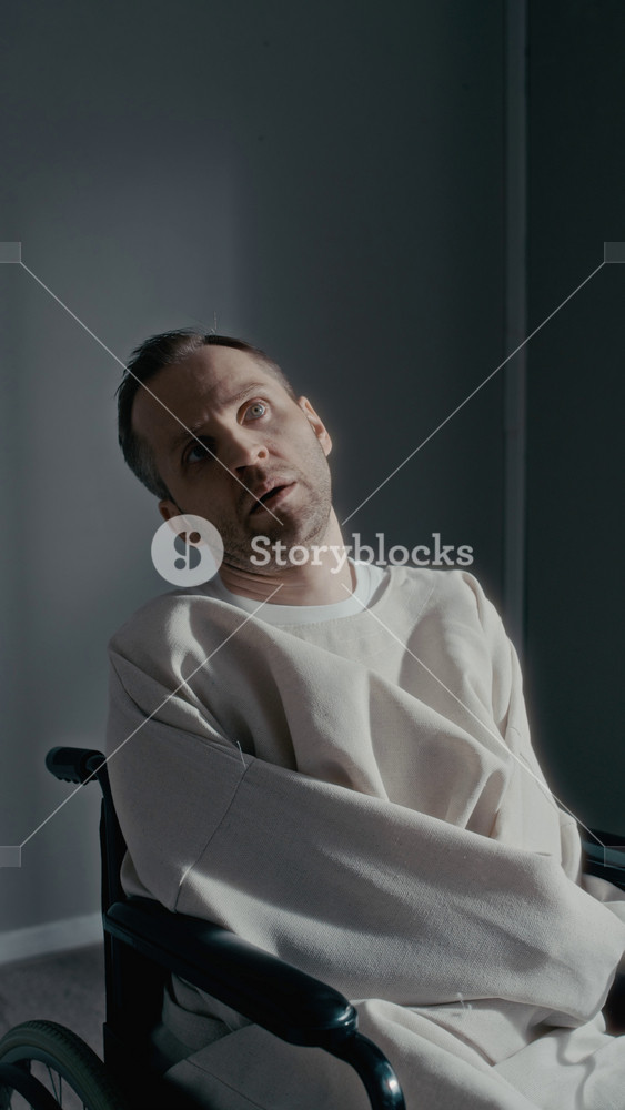 Vertical dolly in portrait of middle aged Caucasian man in straightjacket sitting in wheelchair, staring blankly into camera. Footage is ideal for psychiatric clinic promotions, vertical