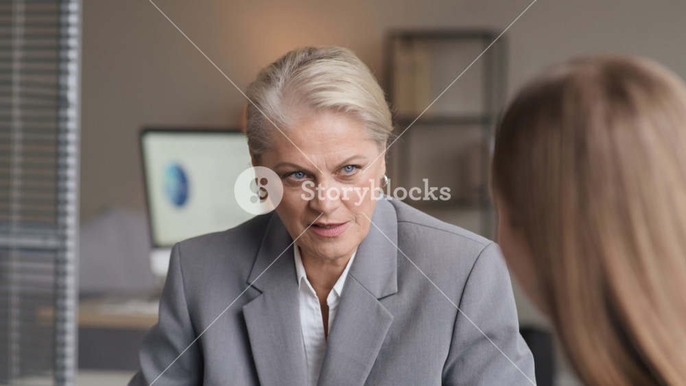 Tilt up shot of confident mature Caucasian female boss sitting at head of conference table and answering questions of female employee during office meeting