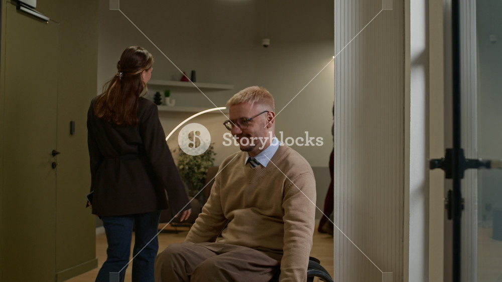 Positive female corporate worker shaking hands with male colleague in wheelchair coming to successful agreement then leaving captured in office hallway