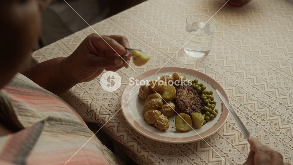 Over shoulder of senior African American woman eating homemade meal of potatoes, peas, and cutlet at dining table. Clip is suitable for senior care, healthy nutrition, and independent living campaigns