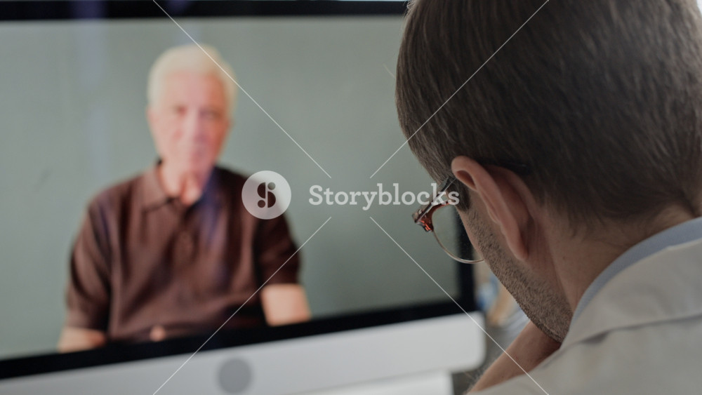 Over shoulder closeup shot of male urologist speaking to senior patient on desktop screen during virtual medical consultation, remote healthcare appointment in professional clinic setting