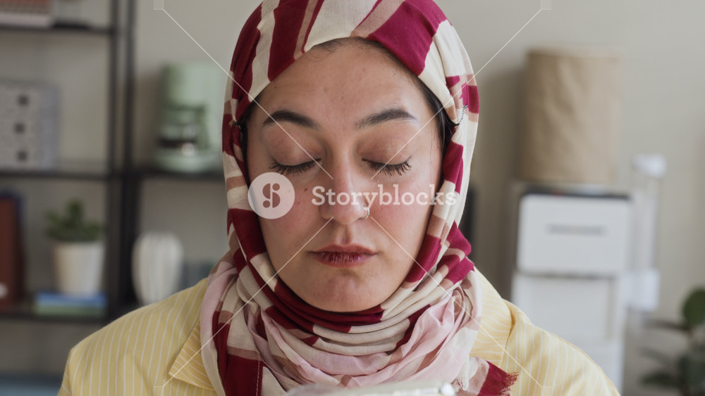 Young adult Middle Eastern woman wearing hijab looking into hand mirror and applying face powder with makeup brush in office. Video suitable for corporate diversity and professional beauty ads