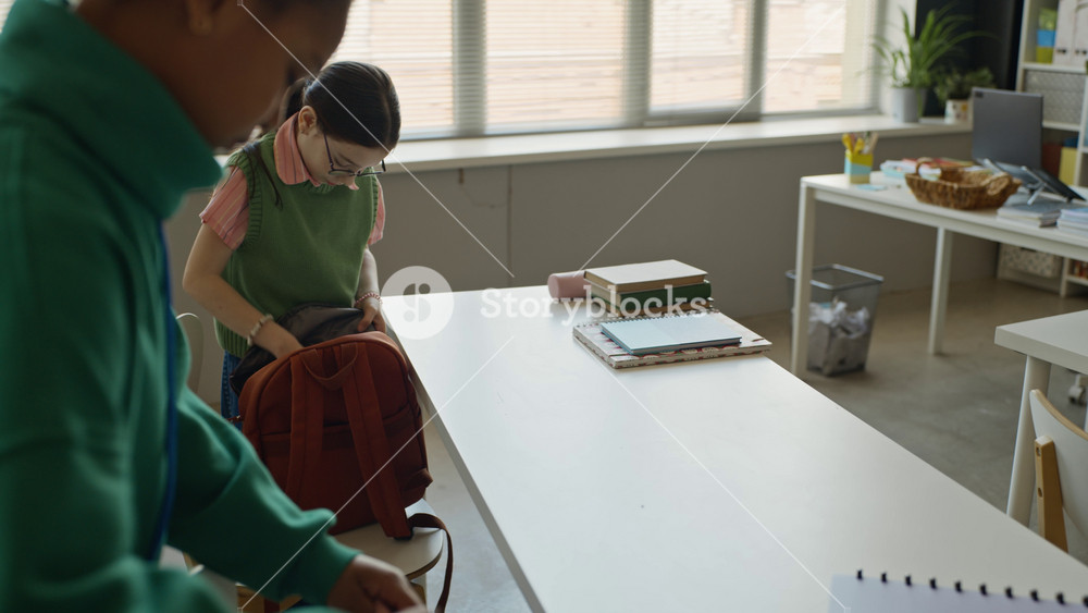 African American and Caucasian teenagers unpacking notebooks from backpacks and placing them on desk in classroom. Perfect for back to school promos and educational marketing