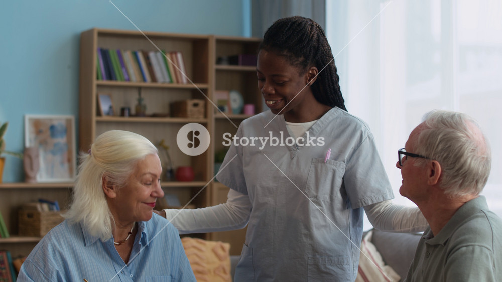 Caring young Black female caregiver serving plate of pastries to elderly residents in nursing home, creating warm and welcoming atmosphere