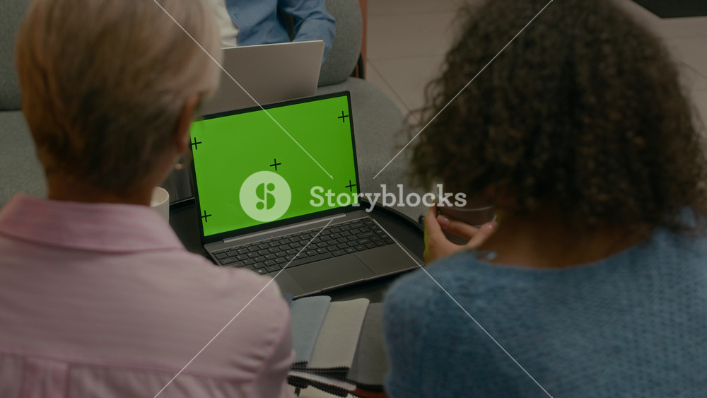 Back view slowmo shot of mature Caucasian female fashion designer and brand manager coworking on choosing fabric color palette while sitting in front of green screen laptop in sleek office