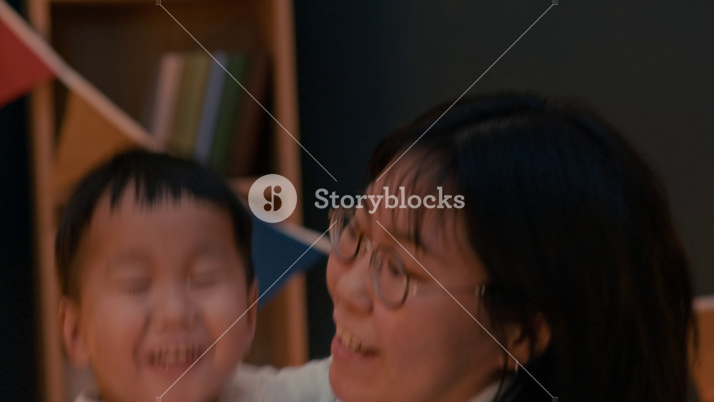 Asian mother holding her little son in arms, sharing playful and joyful moments during bedtime in cozy, warmly lit room, capturing tender family bonding at home