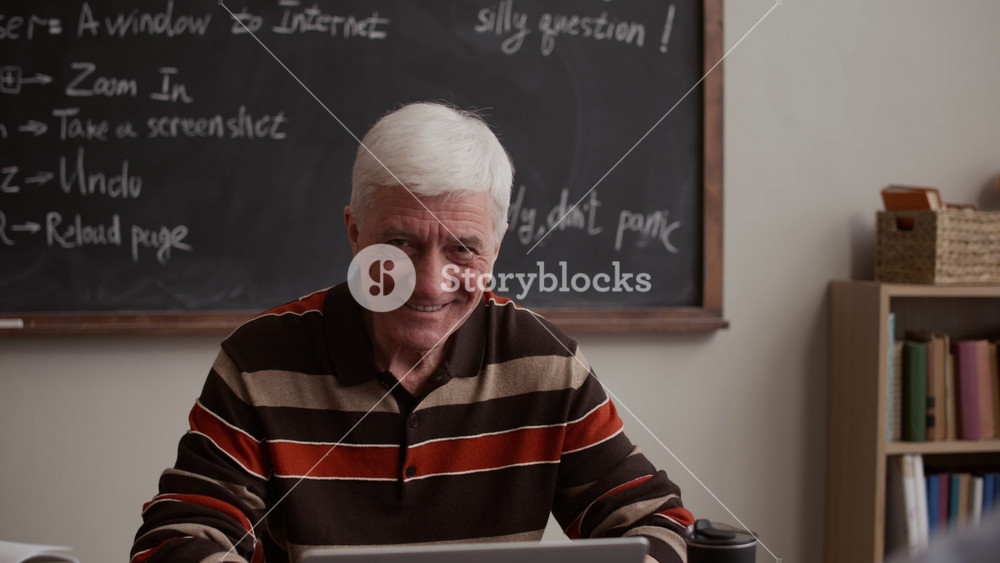 Zoom-in portrait of smiling Caucasian older male student concentrating on laptop use during educational lesson for adults in contemporary classroom with chalkboard in background