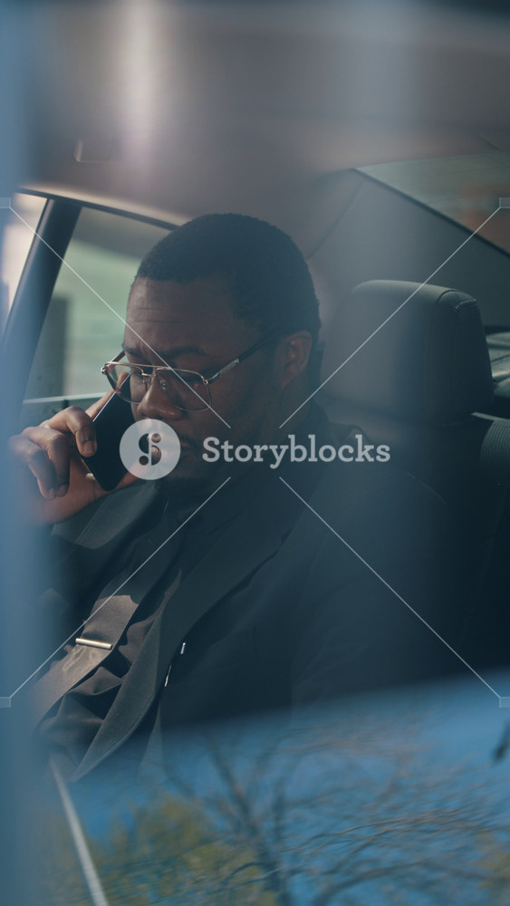 Vertical video of young adult African American businessman in suit talking on smartphone in backseat of moving car. Clip is ideal for corporate communication and mobile business concepts