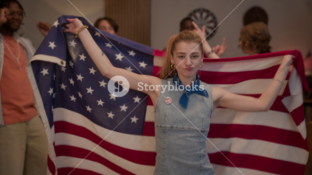 Medium portrait of Caucasian young adult woman dancing with American flag while multiethnic friends celebrate in background. Footage is ideal for Independence Day marketing campaigns