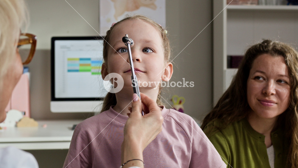 Medium closeup of Caucasian female pediatrician testing eye coordination of Caucasian female child using reflex hammer during medical checkup. Ideal for pediatric healthcare marketing