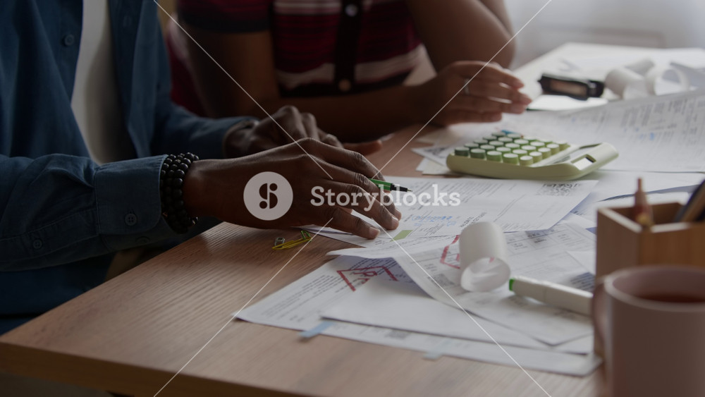 Tilt down slowmo of Biracial couple sitting at home desk reviewing bills and receipts calculating expenses managing household finances or budgeting together