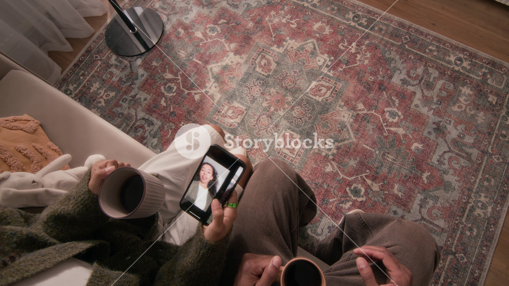 POV shot of caring man bringing to mugs of hot coffee or tea for himself and for his girlfriend, relaxing together on couch in cozy living room during leisure time