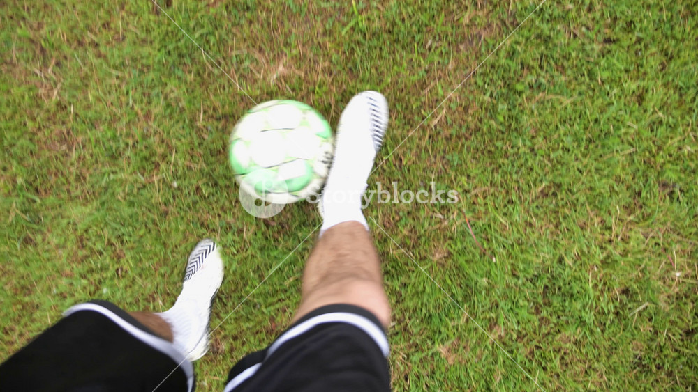 Male feet of professional footballer kicks ball during jogs at meadow on summer day. Legs of sportsman shows tricks with ball while running