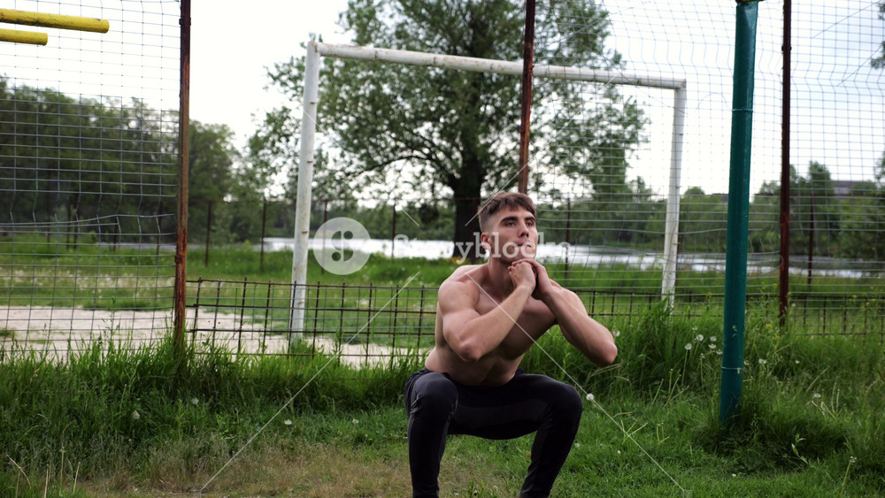 Male shirtless athlete doing squats at sports ground. Young sportsman working at summer nature. Strong sporty man exercising outdoor