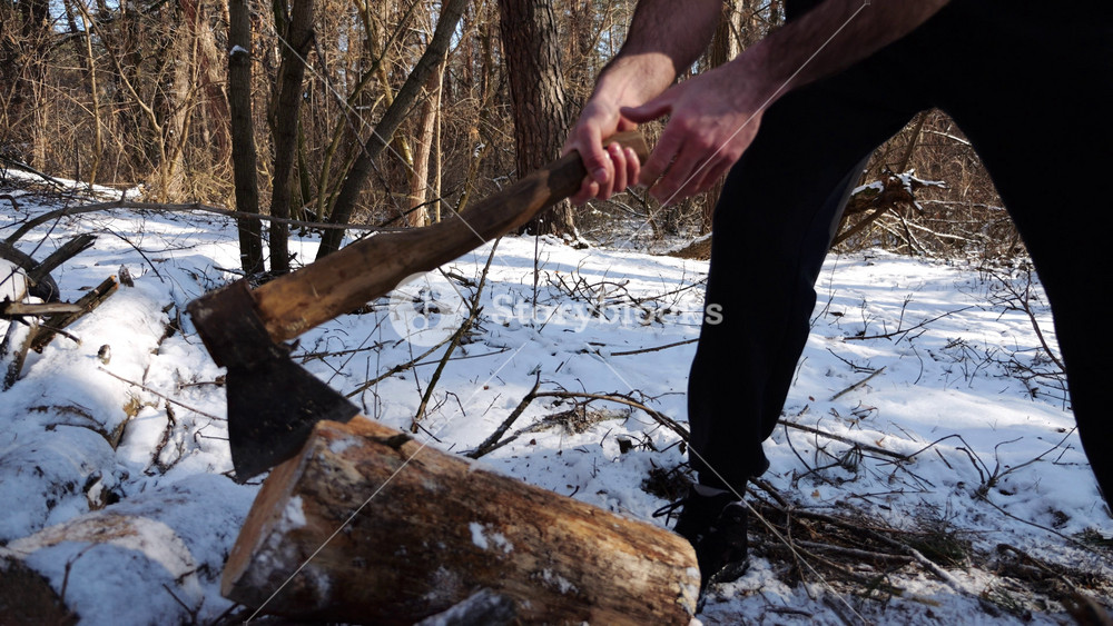 Shirtless young man chopping firewood in a sunny winter forest. Muscular guy working with axe in snowy woodland. Concept of strength