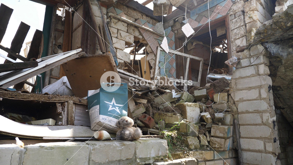 Dirty teddy bear sits beside russian military ration package among wreckage of destroyed home in Ukraine. Symbol of lost innocence contrasts