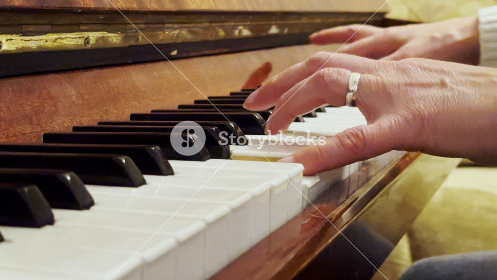 Adult female hands playing a gentle piece of classical music on a brown piano. The scene captures the movement, rhythm and elegance of