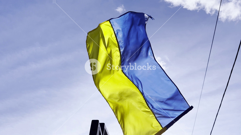 Blue-yellow symbol of Ukraine fluttering at sunny day. Ukrainian flag on flagpole waving at wind against background of sky. Peace and