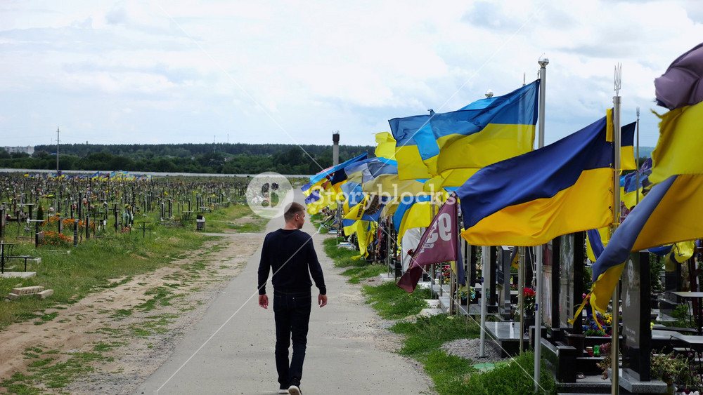 Kharkiv, Ukraine, 2025: Mourning Man walking among countless graves of Ukrainian soldiers with blue-yellow flags at military cemetery in Kharkiv.
