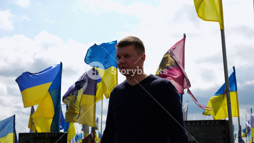 Mourning man standing among countless graves of ukrainian soldiers with national banners pay tribute to fallen family member in Kharkiv