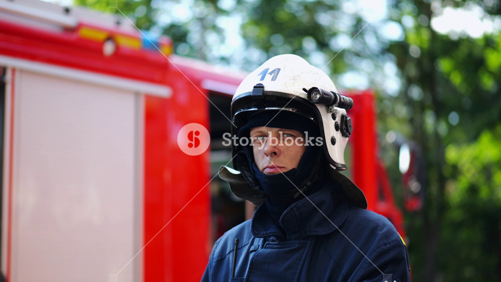 Portrait of confident male fireguard with dirty face standing near a fire engine. Young fireman in full equipment posing after fire against the background of big red truck. Concept of saving lives