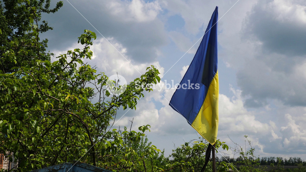 Blue-yellow flag waves proudly on a old fence in Kharkivska oblast. The scene symbolizes the resilience and unbroken spirit of the ukrainian