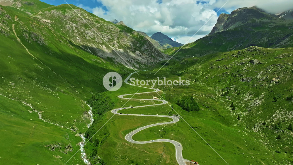 Aerial flyover over the turns of Maloja pass in Swiss. Aerial view of cars on road trip across the mountains of Switzerland drive along hairpin turns. Aerial drone view winding mountain road