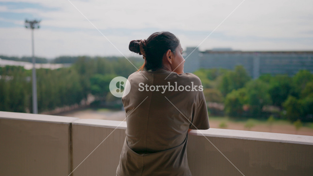 Contemplation on the Balcony. A woman stands alone, gazing out over a cityscape, her back to the camera. The image evokes a sense of introspection and quiet contemplation.