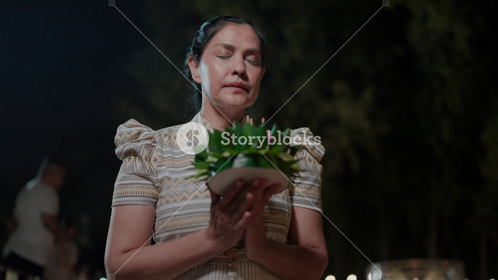 Thai Woman in Traditional Attire Offers Prayers at a Riverside Night Ceremony, Holding a Handmade Krathong as Part of Thailand's Celebrated Cultural Heritage.
