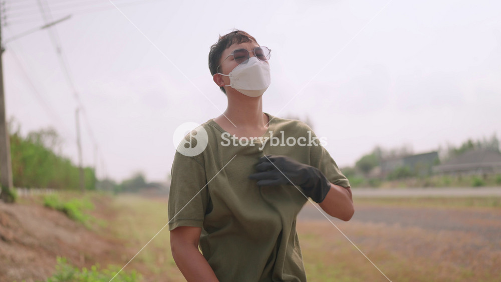An Asian man wearing a face mask, protective glasses, and carrying a hat is seen volunteering to pick up trash on the street, emphasizing the importance of personal safety.