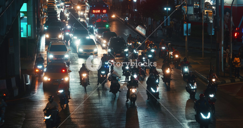 Many cars and motorbikes move slowly in traffic jam in the heavy traffic of the city at night. City traffic, cars and mopeds, busses and