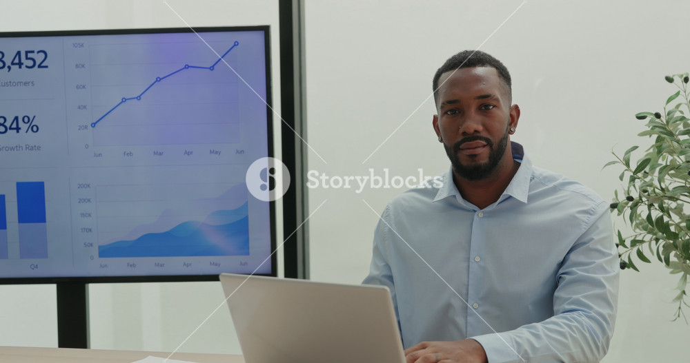 Portrait of African American bearded data analyst works on laptop in office. Financial manager predicts potential profit of deals as sits by