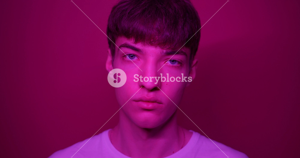 Portrait of Young Millenial Stylish Guy Wearing White T-Shirt Looking Straight to Camera Standing at Futuristic Neon Pink Lights Lifestyle