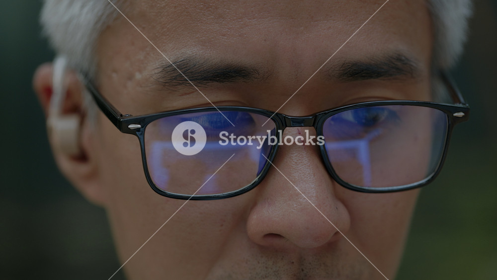 Closeup portrait of mature Asian businessman with hearing aid works on laptop outdoors. Korean corporate employee with disability uses