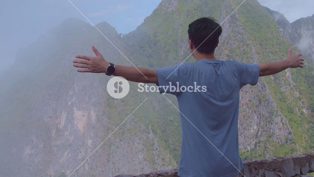 Asian Hiker Male Standing On A Veranda Cliff And Raising His Hands Celebrating Reaching Up Top Of Foggy Mountain