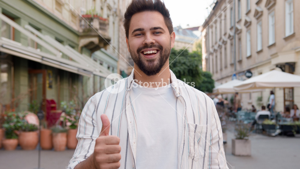 Young Caucasian man posing smiling showing thumb up happy joyful cheerful guy enjoying toothy dental smile satisfaction funny urban city