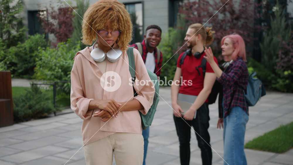 Disappointed African American student girl feeling stress bullying by multiracial students laughing grinning in city upset female woman