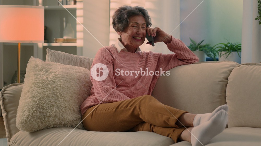 Relaxed happy laughing old woman on cozy sofa talking on smartphone laugh discuss funny news carefree smiling senior grandmother at comfy
