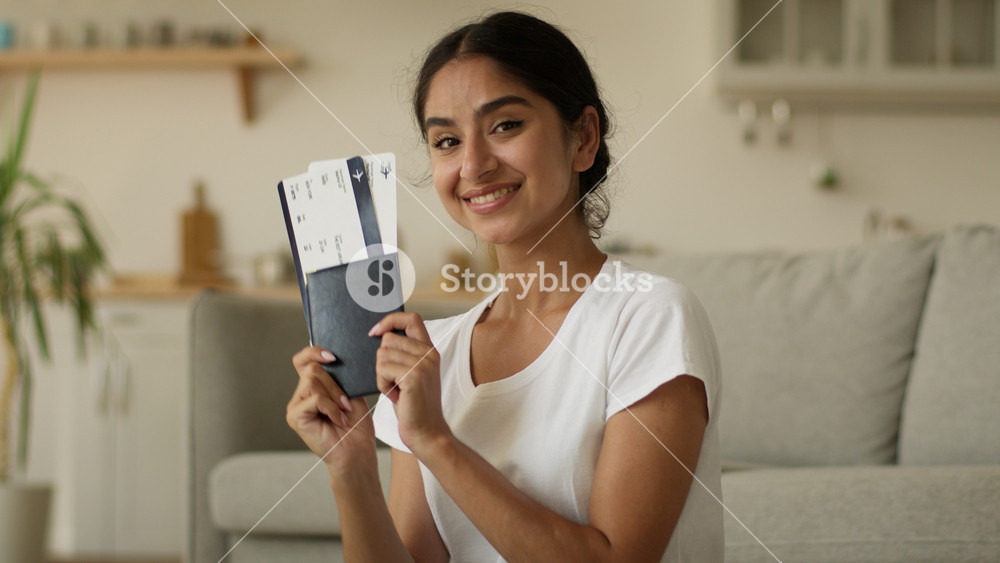 Happy smiling Arabian woman at home Indian girl female traveler tourist holding showing passport travel agency tickets at camera positive