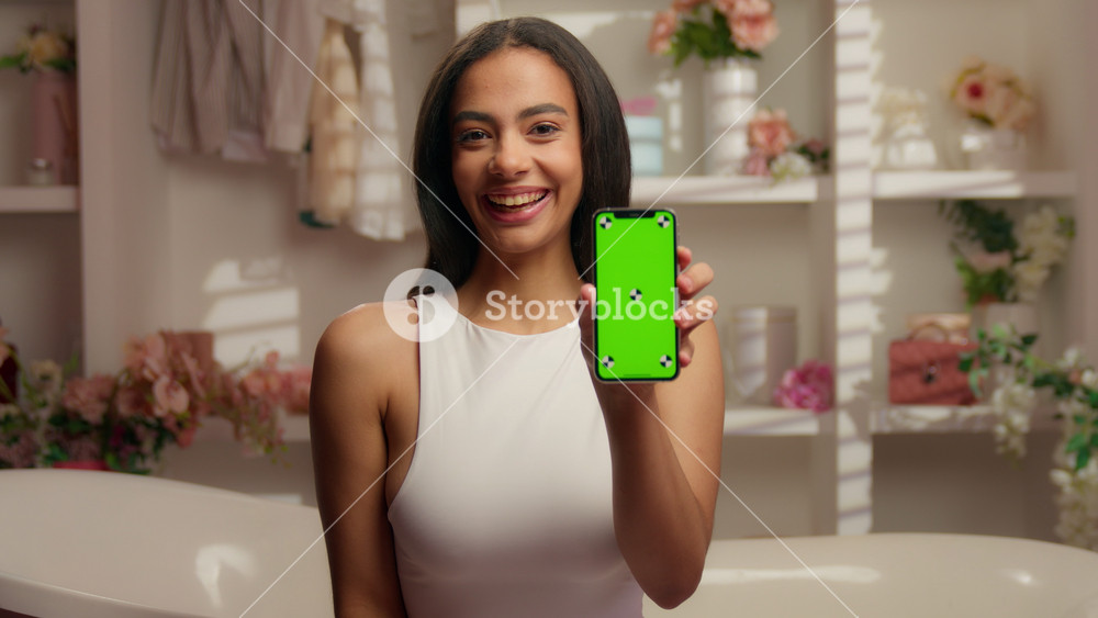 Portrait Hispanic woman showing green screen thumb up recommend online app mobile phone in pink bathroom American girl smile show smartphone