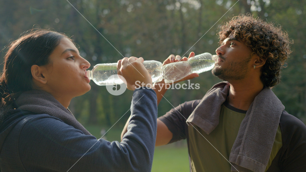 Indian Arabian drink after fitness workout outdoors healthy sport man and woman tired exhausted thirsty after exercise drinking water