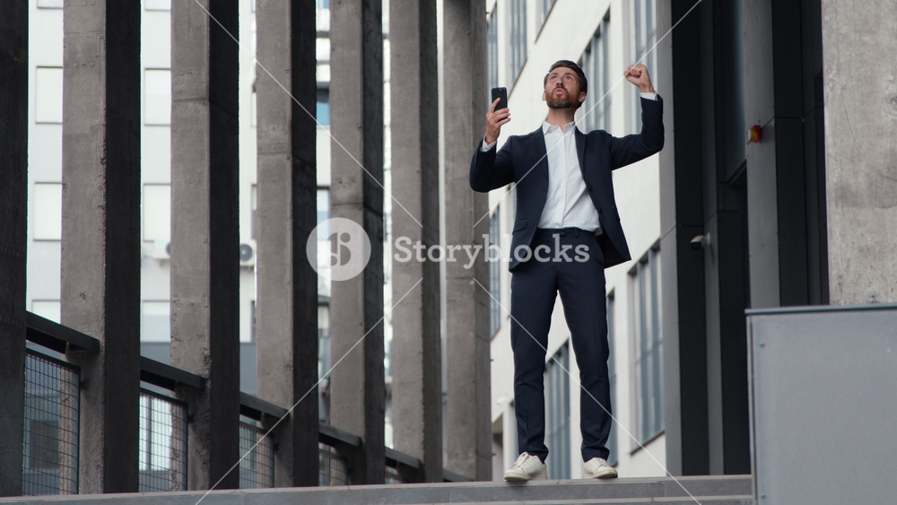 Successful happy mature Caucasian business man businessman win with phone betting jumping celebrating online internet winning male