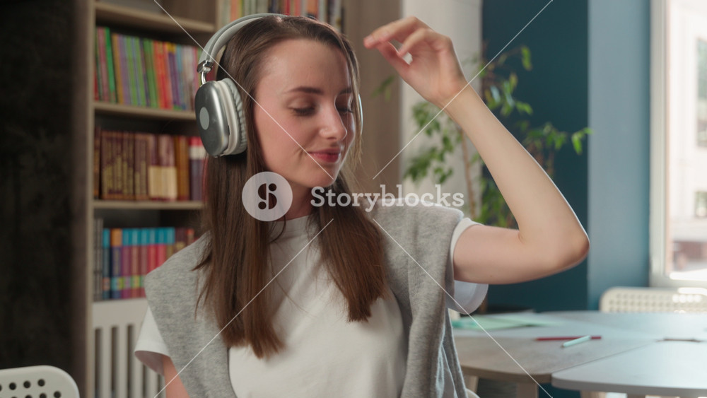 Happy Caucasian woman listening music wireless headphones enjoying playlist in library smiling student female girl learner dancing use
