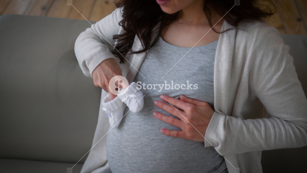 Happy Caucasian mother mom female girl pregnant woman at home couch sofa with booties baby shoes on belly health pregnancy waiting newborn