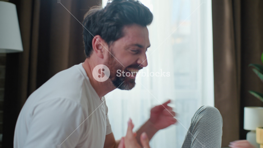 Happy Caucasian family married fooling around having fun tickling laugh in bedroom awaking in morning together. Playful husband man tickle