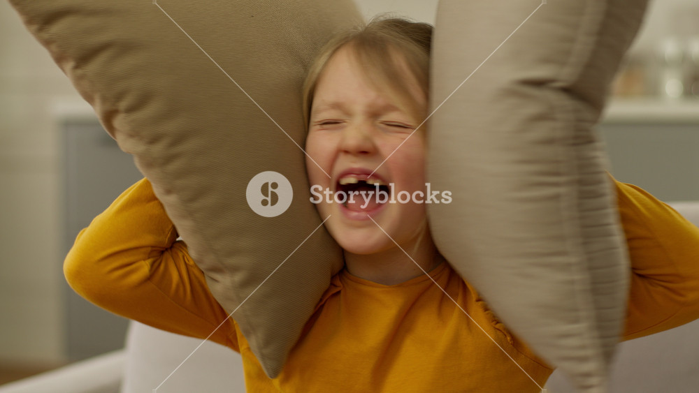 Little Caucasian girl child screaming yelling shouting loud covering ears with pillows protest education daughter offspring displeased anger