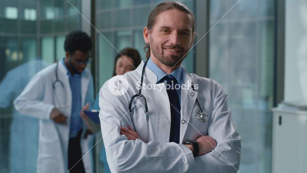 Portrait confident happy Caucasian man doctor smiling posing with crossed hands near medicine workers team colleagues in clinic. Cheerful