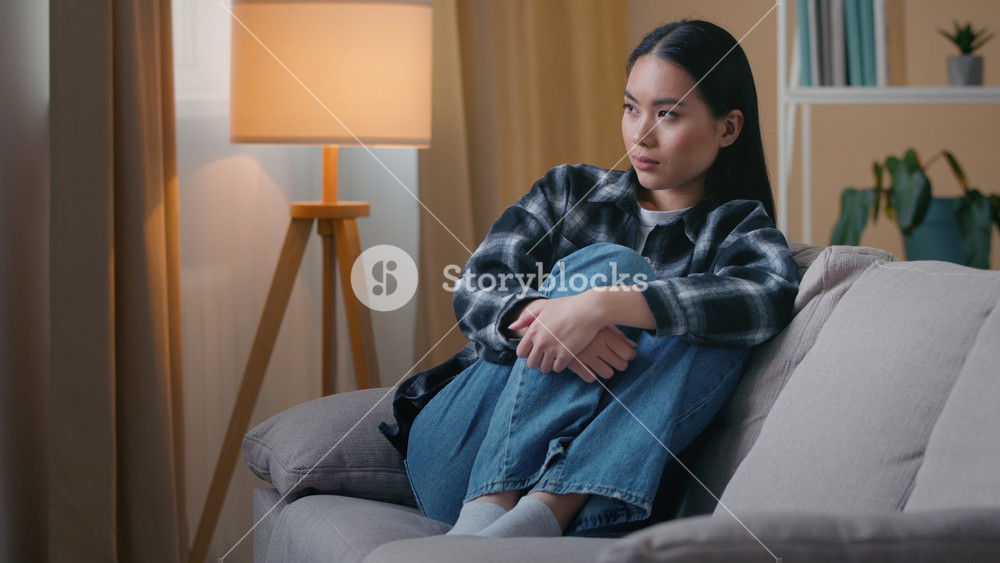 Sad thoughtful Asian woman sit at home upset frustrated Korean female lonely emotional problem bad mood worried troubled girl depression