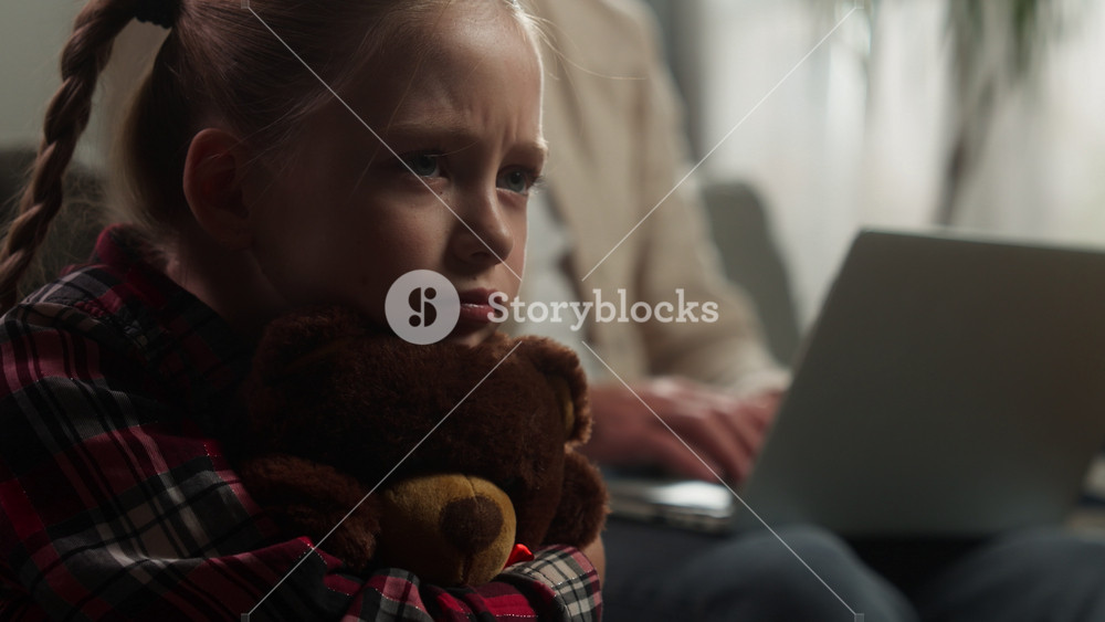 Caucasian upset little girl child hugging teddy bear crying busy father ignoring sad lonely daughter at home dad man male working laptop